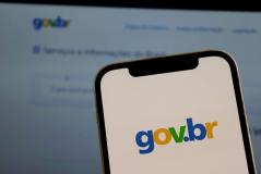 Imagem de um smartphone exibindo o logotipo do site gov.br com fundo borrado da tela de um computador, representando acesso ao portal oficial do governo brasileiro.