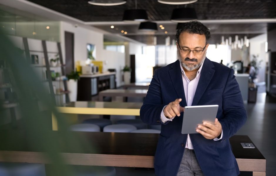 Executivo de negócios usando tablet em um ambiente de escritório moderno e bem iluminado, representando inovação no mercado de trabalho.