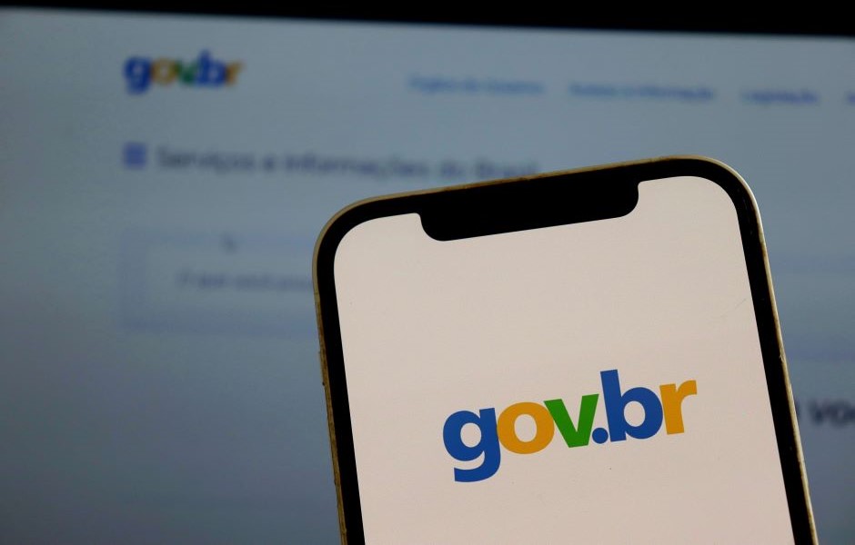 Imagem de um smartphone exibindo o logotipo do site gov.br com fundo borrado da tela de um computador, representando acesso ao portal oficial do governo brasileiro.