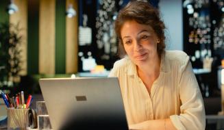 Mulher sorridente trabalhando em seu laptop em um ambiente moderno, com iluminação agradável e decoração contemporânea, ideal para produtividade.