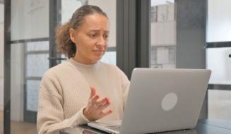 Mulher com expressão de dúvida ou confusão, usando um celular e um laptop, em ambiente de escritório moderno, representando dificuldades ou desafios no trabalho, relevante para o tema de problemas profissionais ou tecnológicos.