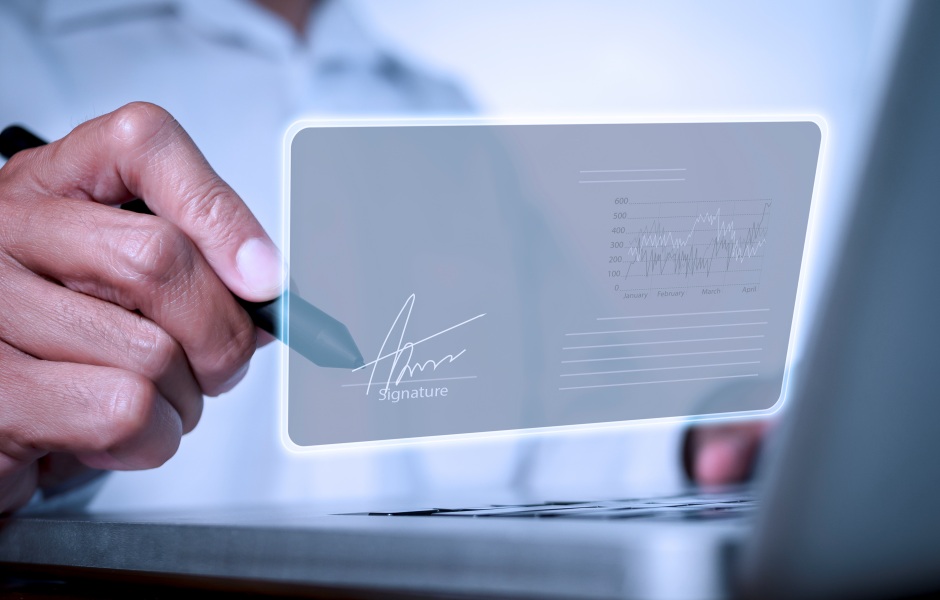 Mão masculina assinando digitalmente uma tela holográfica com gráfico de dados ao fundo.