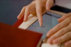 Pessoa usando smartphone para fazer assinatura digital, sentado em mesa com documentos ao redor, rotina de trabalho ou assinatura digital.