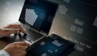 Mãos operando um notebook e segurando uma caneta digital ao lado de um tablet. Telas e fundo exibem elementos gráficos transparentes conectados, representando gerenciamento de arquivos, pastas virtuais e bancos de dados.