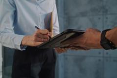 Pessoa segurando um tablet enquanto outra pessoa faz anotações durante uma reunião de negócios.