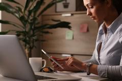 Mulher em escritório utilizando tablet para realizar assinatura eletrônica em documentos digitais, transmitindo segurança e validade jurídica no ambiente corporativo.