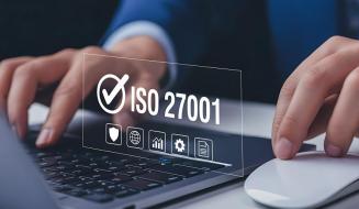 Close-up das mãos de uma pessoa usando um notebook e mouse, com uma sobreposição digital do selo de certificação ISO 27001 e ícones de segurança cibernética.