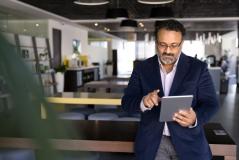 Executivo de negócios usando tablet em um ambiente de escritório moderno e bem iluminado, representando inovação no mercado de trabalho.