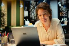 Mulher sorridente trabalhando em seu laptop em um ambiente moderno, com iluminação agradável e decoração contemporânea, ideal para produtividade.