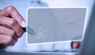 Mão masculina assinando digitalmente uma tela holográfica com gráfico de dados ao fundo.