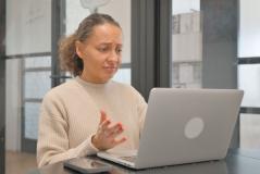 Mulher com expressão de dúvida ou confusão, usando um celular e um laptop, em ambiente de escritório moderno, representando dificuldades ou desafios no trabalho, relevante para o tema de problemas profissionais ou tecnológicos.