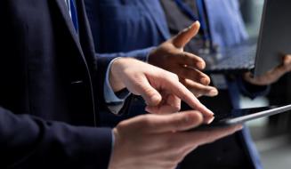 Profissionais de terno utilizando tablet e notebook em ambiente corporativo.