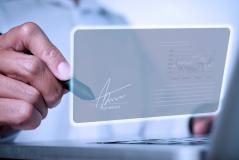 Mão masculina assinando digitalmente uma tela holográfica com gráfico de dados ao fundo.